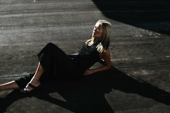 Blonde woman wearing a black dress resting on a dark paved surface outdoors in Sydney