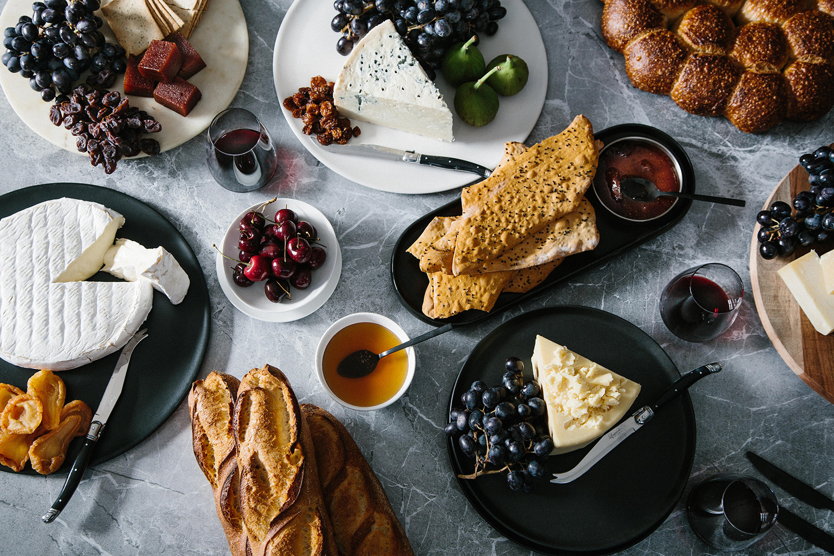 Overhead shot of an abundant charcuterie board featuring various cheeses, fruits, breads, and crackers arranged on a gray marble surface.