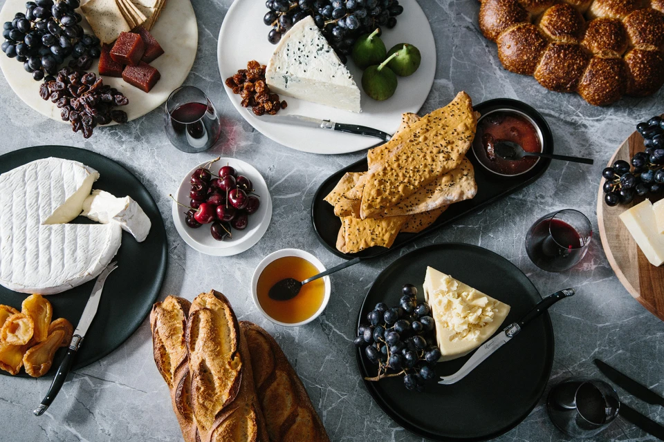 Overhead shot of an abundant charcuterie board featuring various cheeses, fruits, breads, and crackers arranged on a gray marble surface.