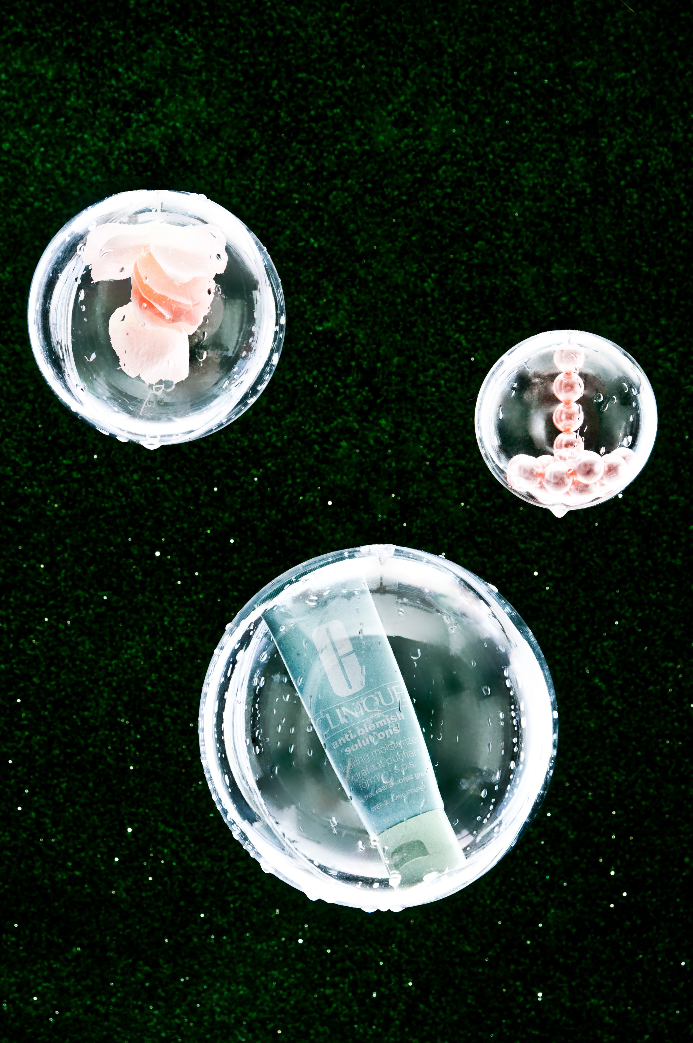 Still life product shot of Clinique moisture surge skincare tube in a petri dish with skincare samples on a dark green background.