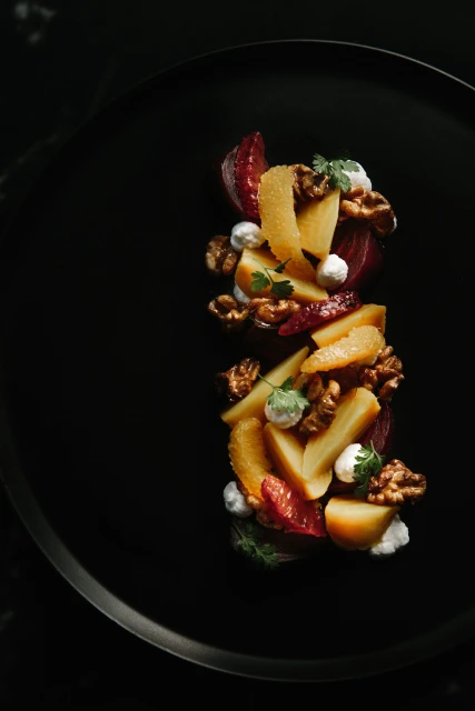 Overhead shot of a black plate presenting a gourmet salad with beetroot, pear slices, walnuts, white cheese, and parsley garnish.
