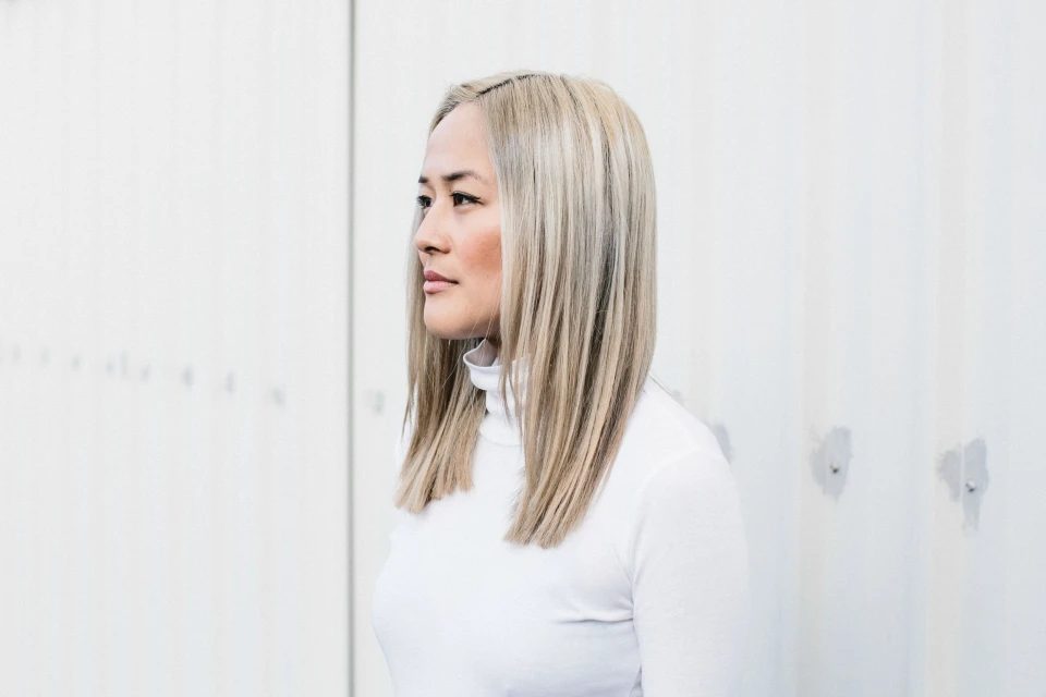 Profile portrait of a blonde woman in a white turtleneck against a plain white wall, showcasing a clean and minimalist aesthetic.