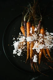 Roasted whole carrots topped with crumbled white cheese and spices on a dark plate.