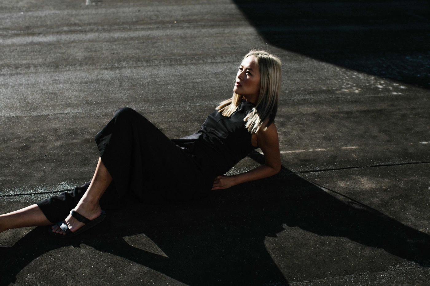 Blonde woman wearing a black dress resting on a dark paved surface outdoors in Sydney