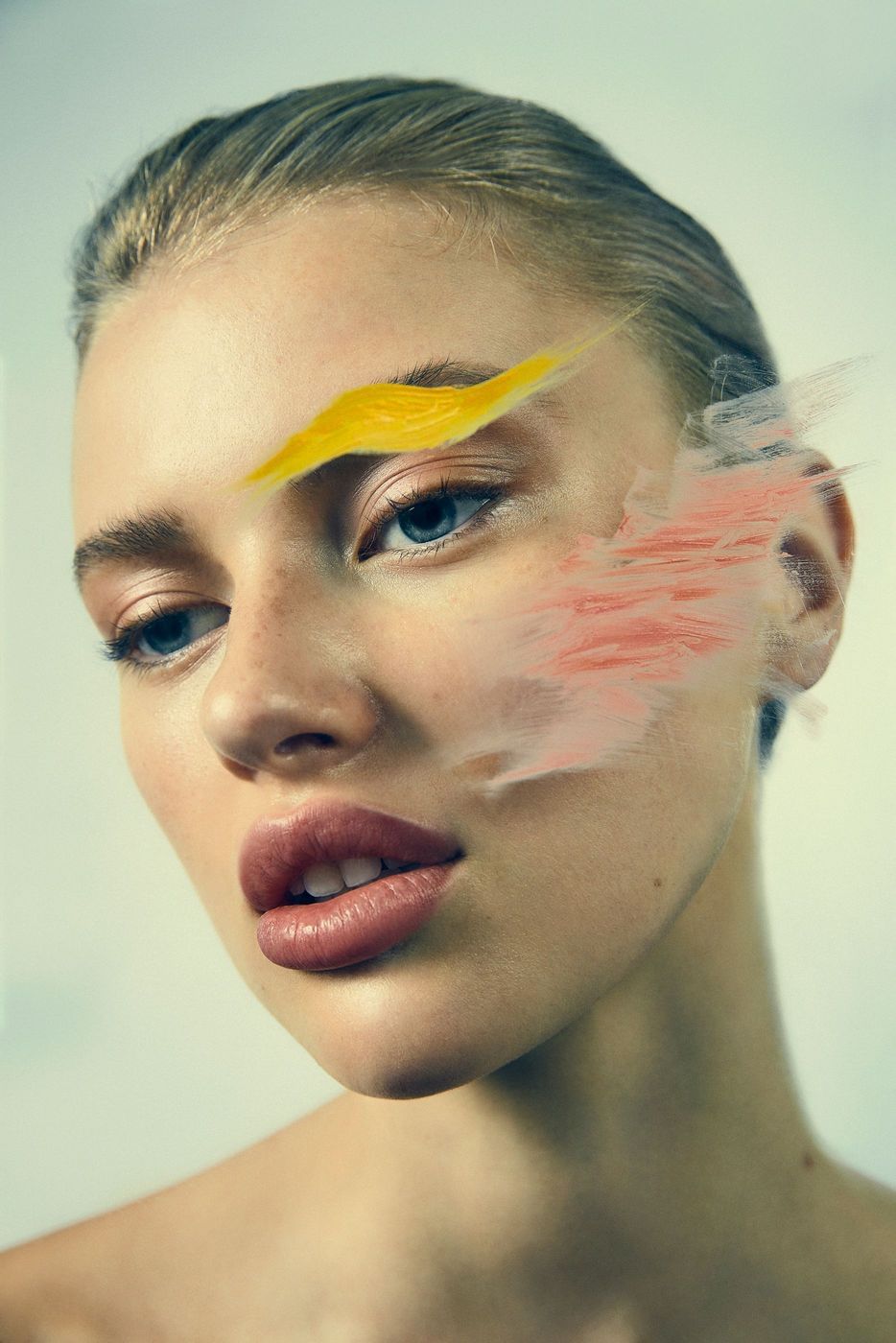 Close-up portrait of a fair-skinned woman with artistic feather accents on her face against a neutral background, beauty concept.