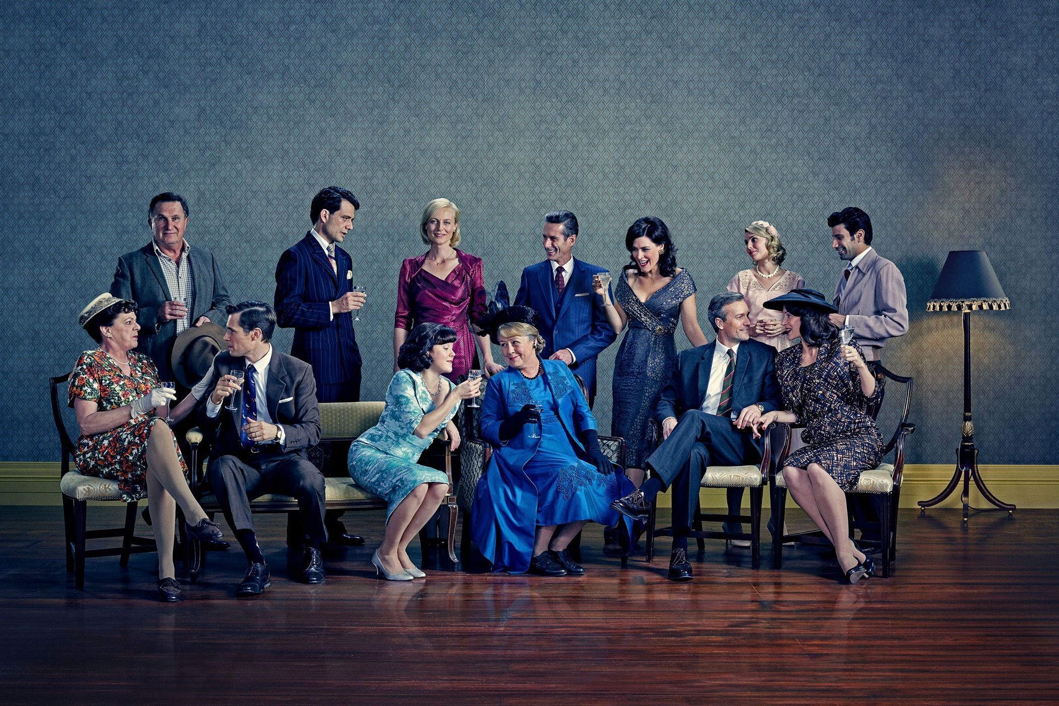 Group portrait of eleven people dressed in formal mid-century attire sitting and standing in an indoor setting, holding glasses.