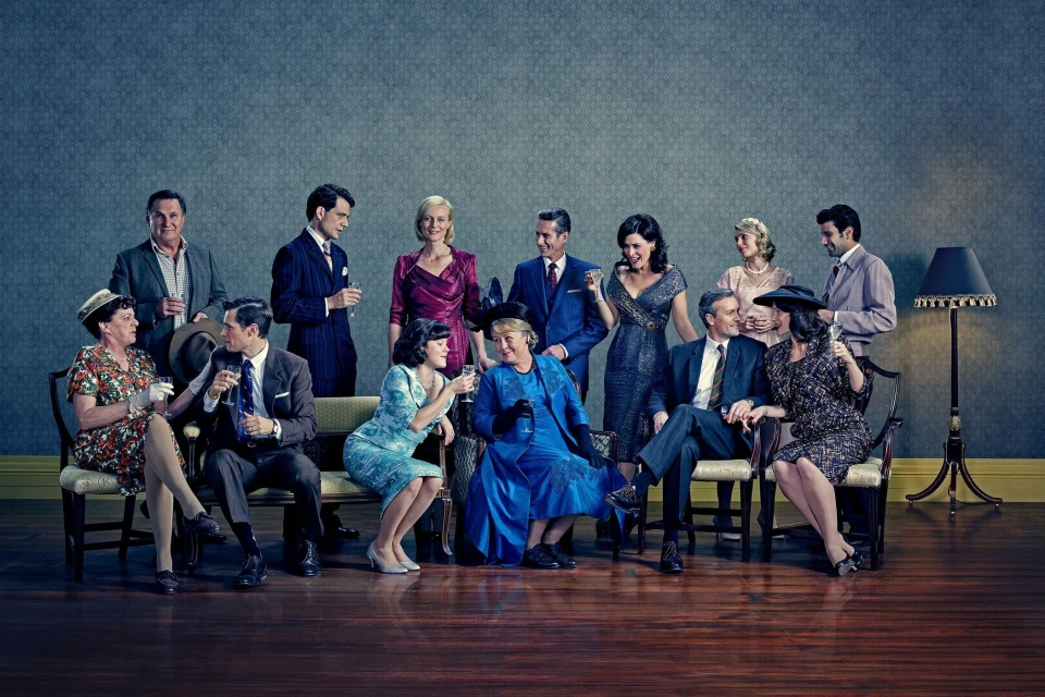 Group portrait of eleven people dressed in formal mid-century attire sitting and standing in an indoor setting, holding glasses.