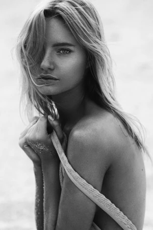Black and white portrait of a woman with long hair looking at the camera on a sandy beach
