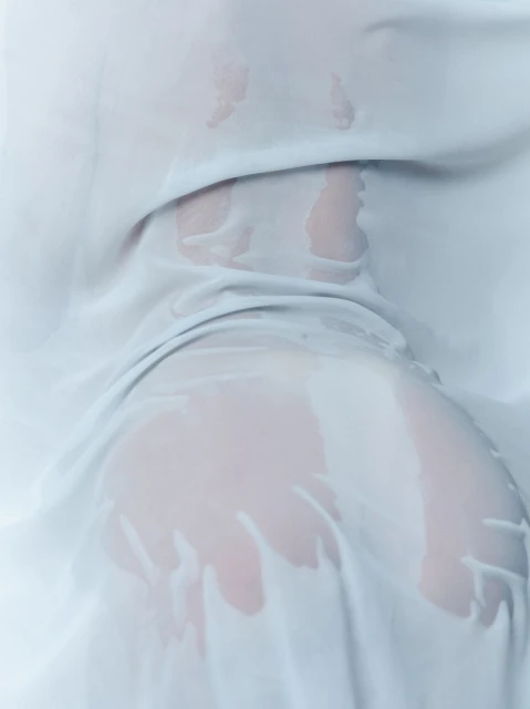 A close-up studio shot of a human form draped in flowing white fabric with water droplets, creating soft textures and shadows.