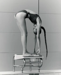 Monochrome image of a female swimmer bending backward over a starting block wearing a patterned swimsuit.