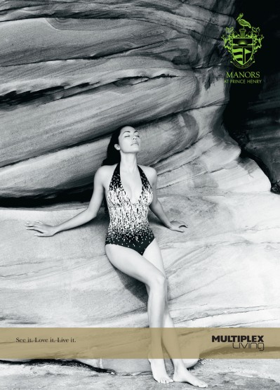 Woman in one-piece swimsuit lying on her back against a rock formation, eyes closed, outdoors, natural light, monochrome, advertisement for Manors at Prince Henry.