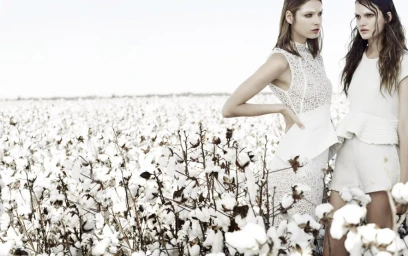 Two female models in white textured apparel standing in a cotton field under an overcast sky by Corrie Bond
