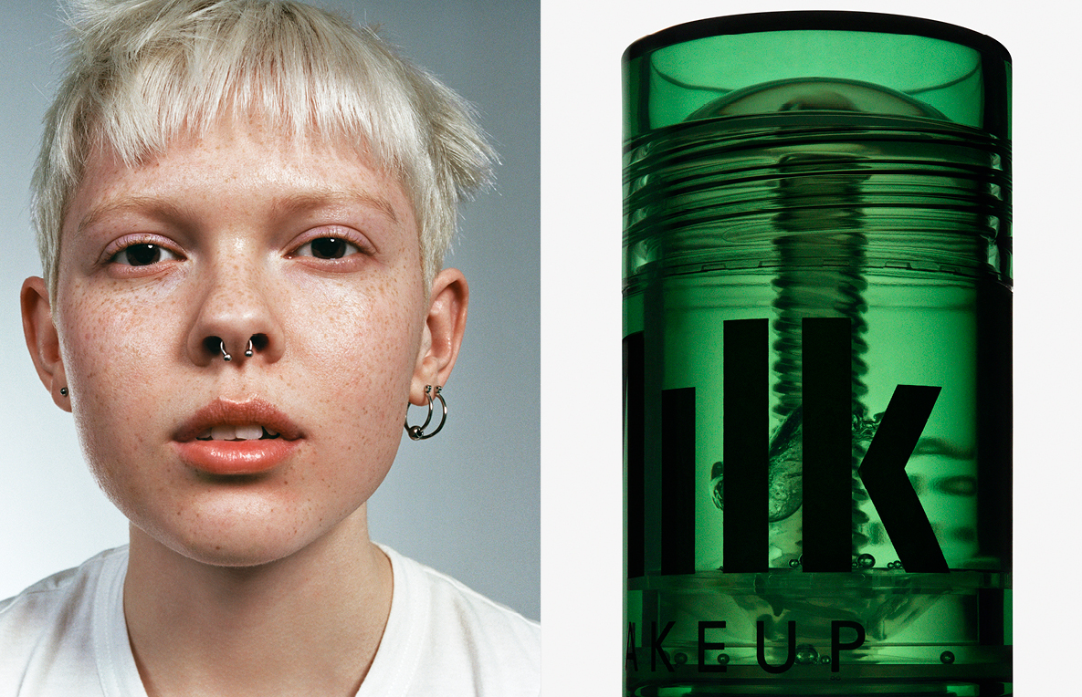 Close-up studio shot of a person with short blonde hair, a nose ring, silver hoop earrings, next to green cosmetic product with black text.