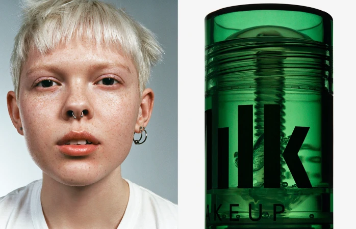 Close-up portrait of a person with short blonde hair and freckles next to a green Milk Makeup product container.