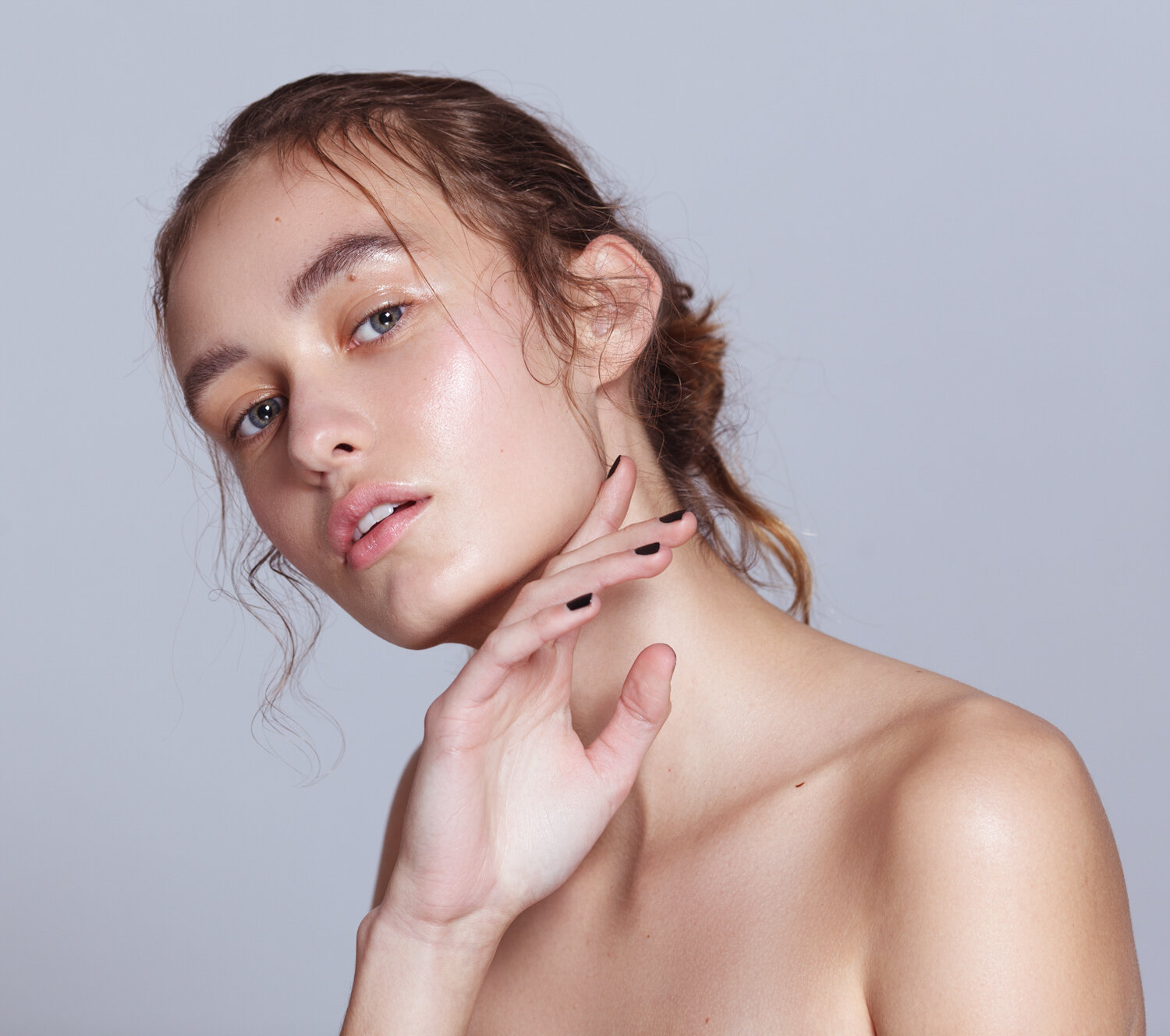 A young woman with wet-look hair and makeup poses against a gray background, showcasing her bare shoulders and neck in a beauty shot.