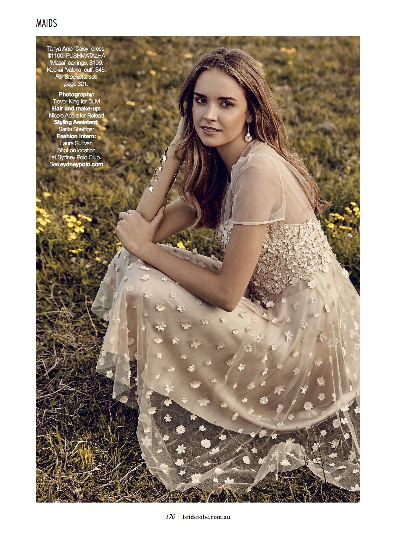 A young woman in a floral dress sits in a field of yellow flowers. The image has a warm, natural lighting and shallow depth of field.