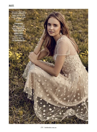 Model in sheer cream floral applique dress squatting in a grassy field with yellow wildflowers