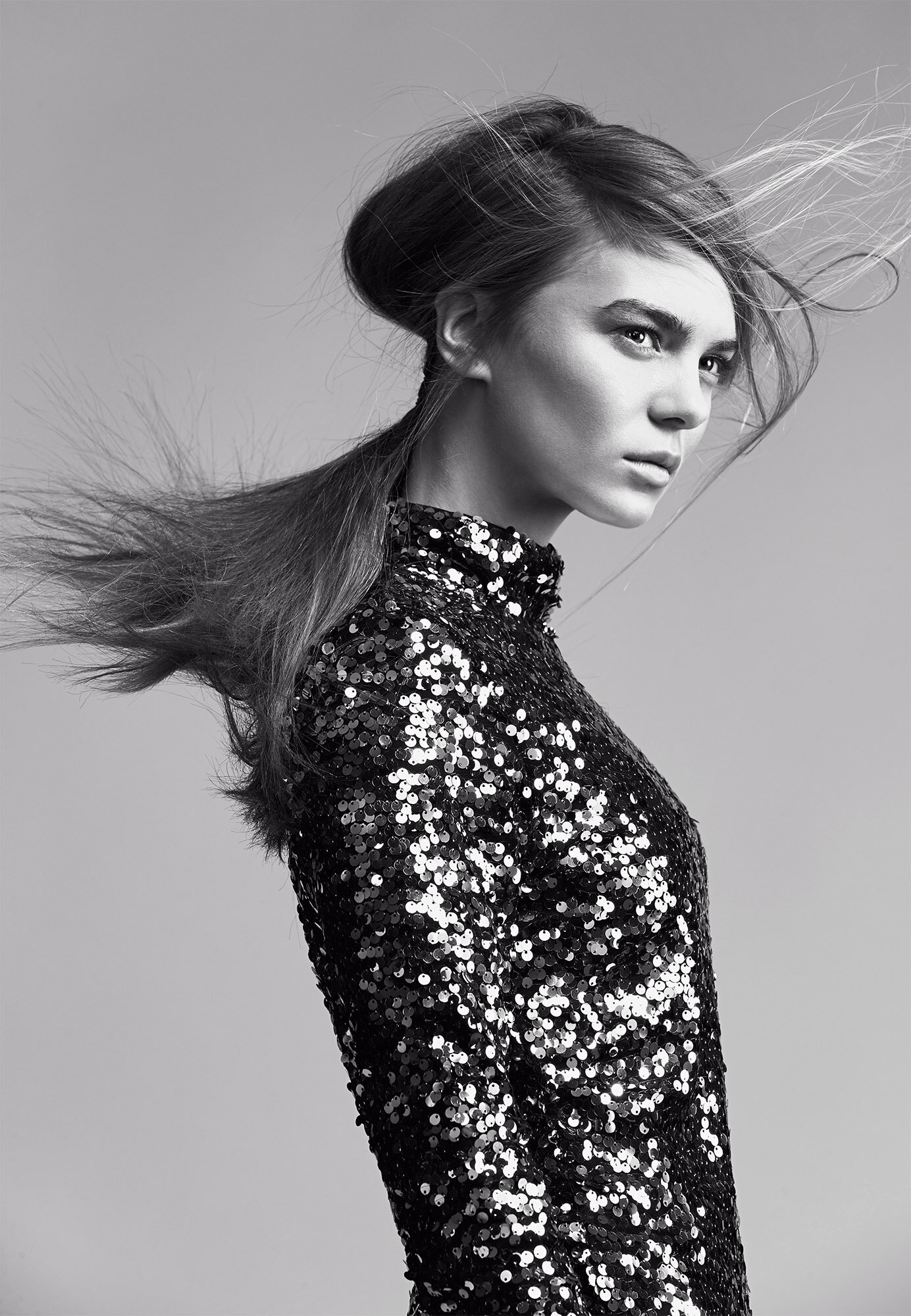 Model in a black sequin dress with hair blowing across her face against a grey backdrop, styled by Nicole Abela.