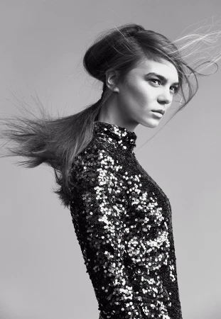 Model in a black sequin dress with hair blowing across her face against a grey backdrop, styled by Nicole Abela.