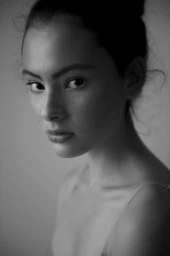 Close-up portrait of a woman with her hair in an updo, looking seriously at the camera against a neutral background.
