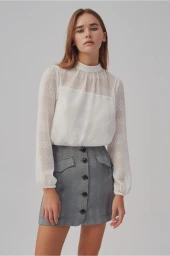 A female model wearing a white sheer patterned blouse and a grey plaid miniskirt against a plain studio background.