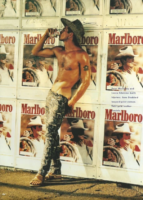 Shirtless man in a cowboy hat drinks from a can, leaning against a wall of Marlboro ads in an outdoor setting, tan sandals.