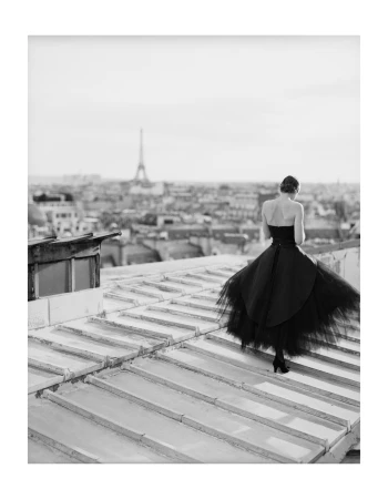 Woman in a black strapless gown standing on a rooftop overlooking Paris with the Eiffel Tower in the distance.
