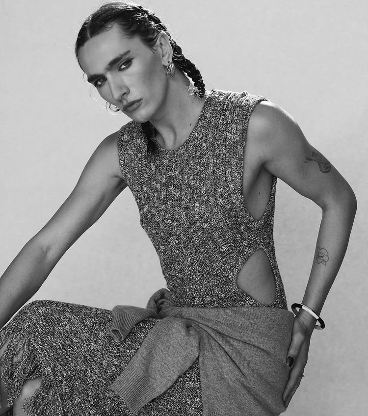 Black and white portrait of an adult with braids, wearing a sleeveless knit dress with cutouts and sweater tied at the waist.