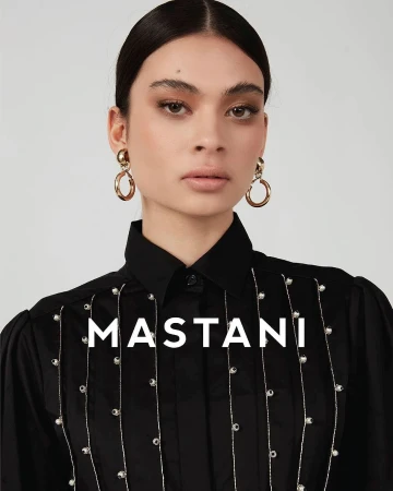 Close-up portrait of a woman wearing a black button-down shirt adorned with vertical pearl chains and gold hoop earrings.