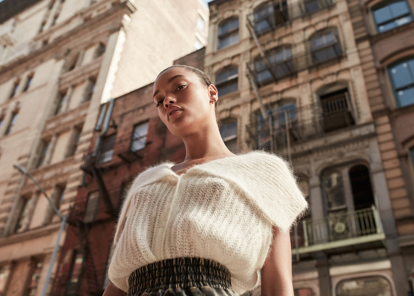 Eye-level shot of a young woman in a white sweater in an urban setting, showcasing fashion and city lifestyle.
