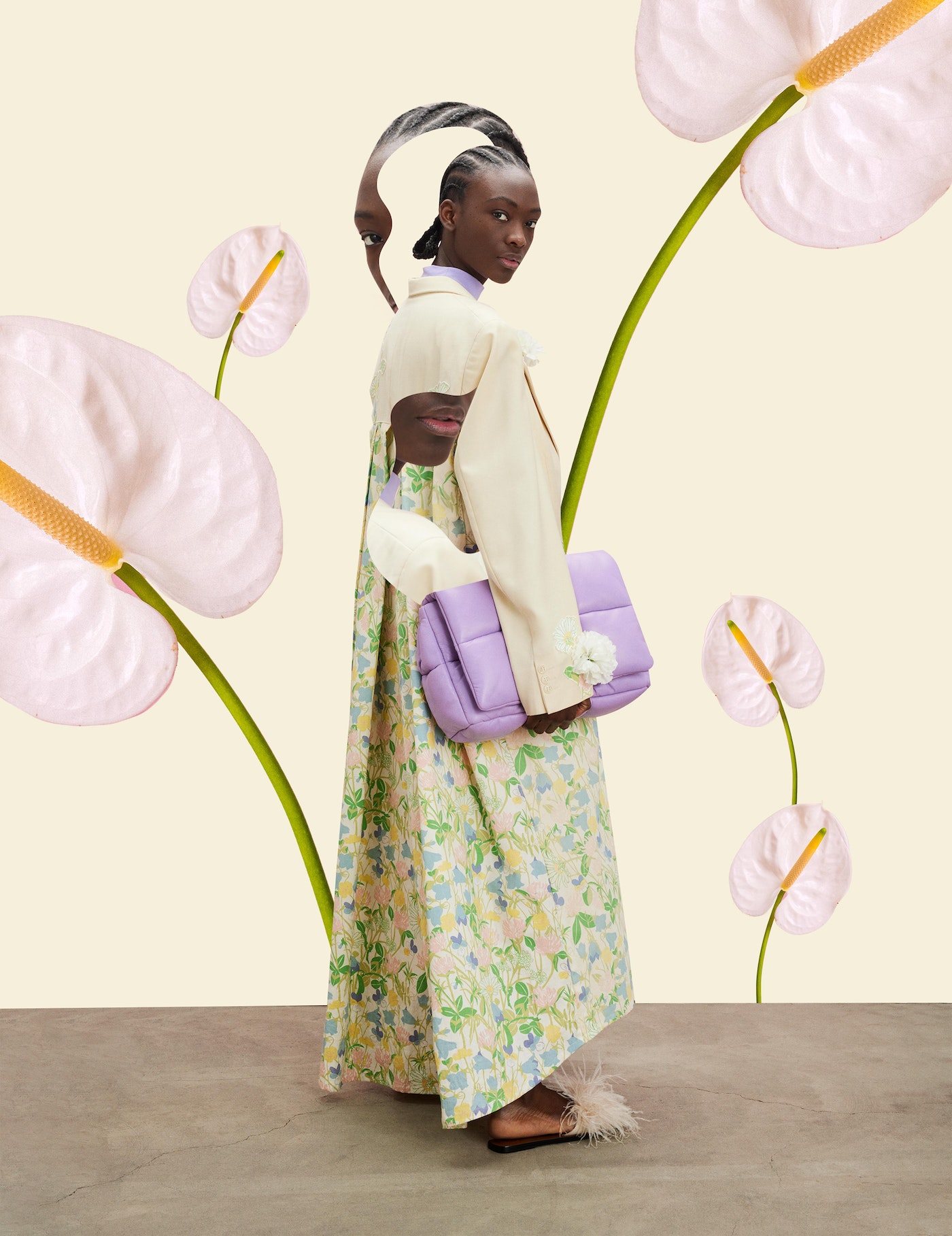 A Black fashion model poses in a dress with a floral pattern while holding a lavender purse, complemented by calla lilies in the background.