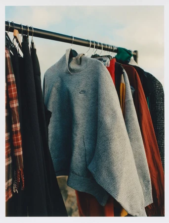 Clothing rack with a gray Nike sweatshirt, various jackets, and garments against a blurred outdoor background under an overcast sky.