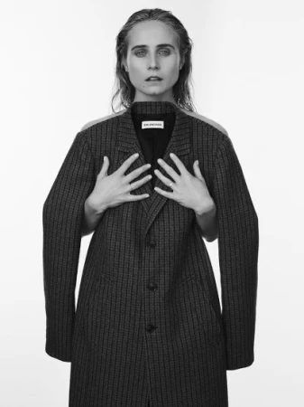 Black and white portrait of a woman wearing a plaid coat held up with visible hands by another person from behind.