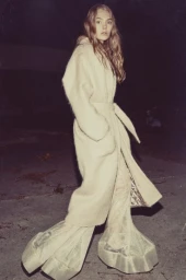 Model in fluffy cream coat and wide translucent trousers walking outdoors at night