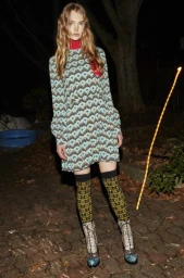 Model in patterned minidress and knee-high socks standing on paving stones outdoors at night, shot by Michael Naumoff.