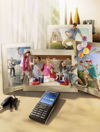 Mobile phone on a table with framed photos of diverse activities and tourist destinations; family celebration, ice skating, Paris, amusement park.