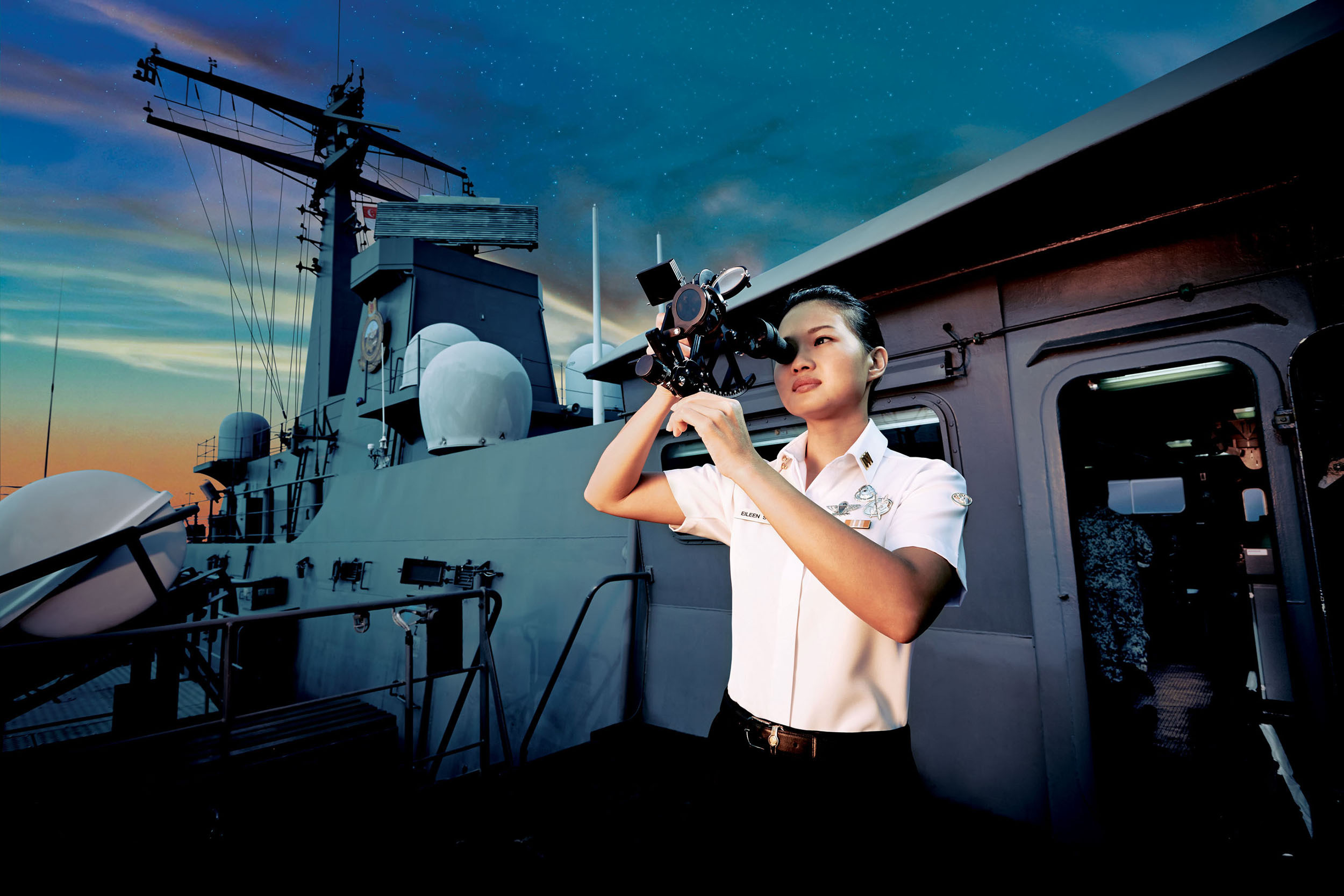 Woman using a sextant on a naval ship. She wears a white collared shirt and dark pants. The ship has radar equipment and life rafts.