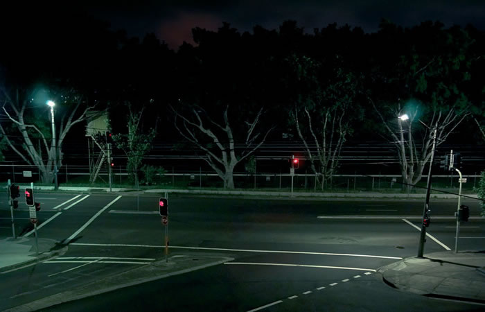 Nighttime street view of a quiet intersection with streetlights illuminating crosswalks, trees, and traffic signals with red lights.