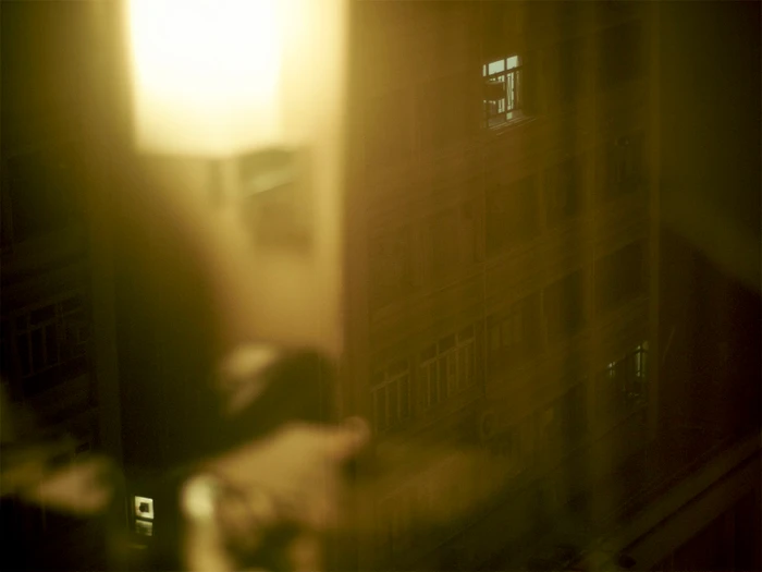 Moody low-angle exterior view of an urban building at dusk shot through a glowing window with warm reflections.