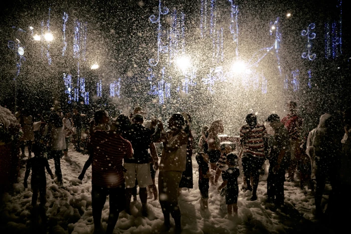 A crowd of people enjoying an outdoor nighttime celebration amidst heavy falling snow illuminated by overhead lights.