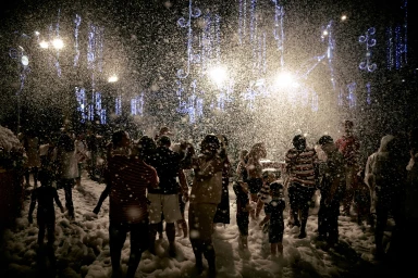 A crowd of people enjoying an outdoor nighttime celebration amidst heavy falling snow illuminated by overhead lights.