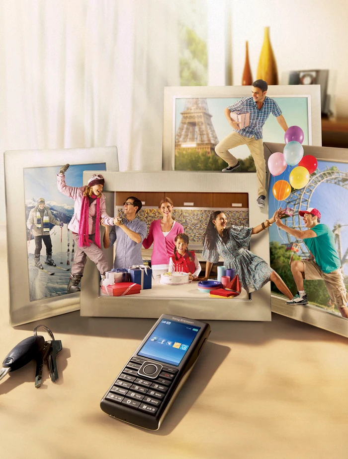 A mobile phone resting on a table surrounded by multiple picture frames displaying scenes with people interacting.