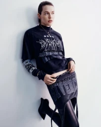 Model in graphic black t-shirt and skirt leaning against a white studio wall with dark boots