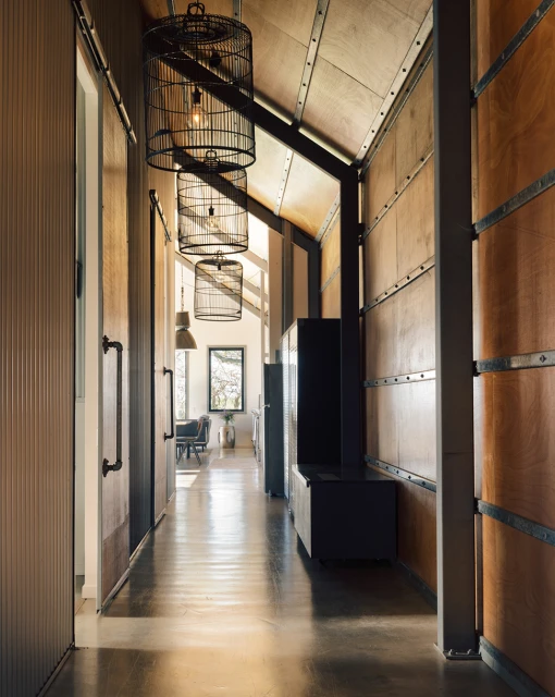 Indoor hallway with hardwood floors and walls, featuring three decorative birdcage pendant lights hanging from the ceiling and neutral colors.