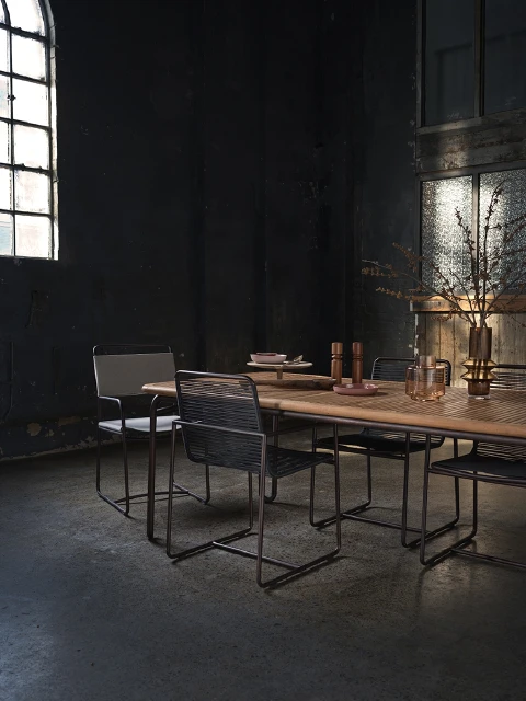 Contemporary dining room with a light wood table surrounded by metal chairs, set against a dark, moody interior and natural light.