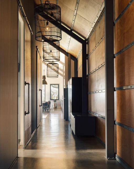 Hallway interior with three black, birdcage-style pendant lights hanging from the ceiling, doors on the left, and paneled walls.