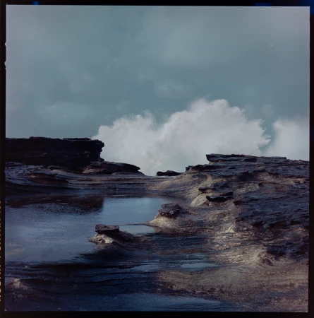 Coastal rock formations and crashing waves under a cloudy sky, creating a dramatic seascape with textured rock details and dynamic water motion.