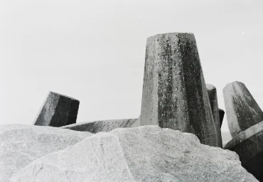 Monochrome low-angle shot of large concrete tetrapods and stacked granite boulders against a pale overcast sky.