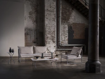 Modern metal frame sofa and matching armchairs with neutral beige cushions arranged in a rustic industrial warehouse space.