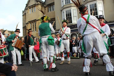 Group of Morris dancers in traditional white trousers, green sashes, and flower-adorned top hats performing on a street in Sydney